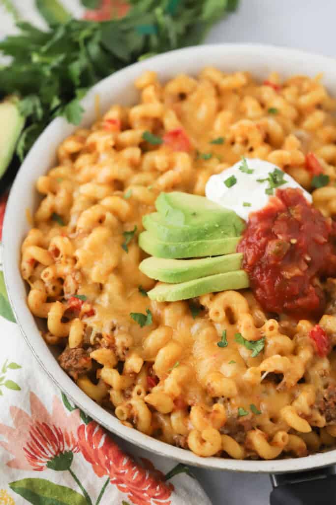 A big bowl of this taco pasta recipe, topped with sliced avocados, salsa, and sour cream.