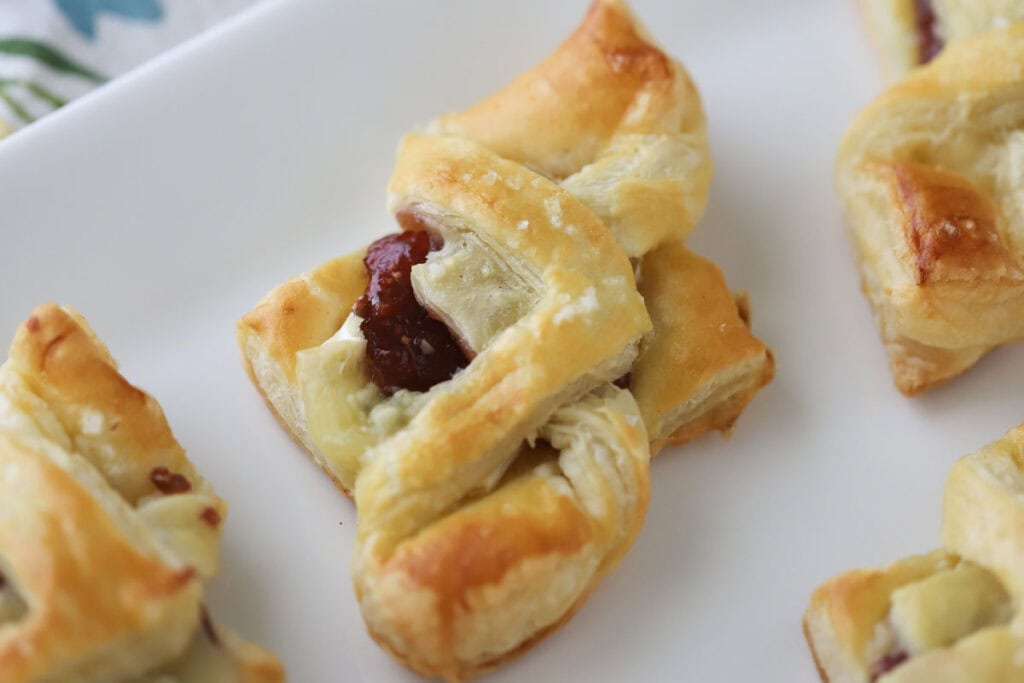 Brie cheese bites with fig jam and gorgonzola cheese on a white serving platter.