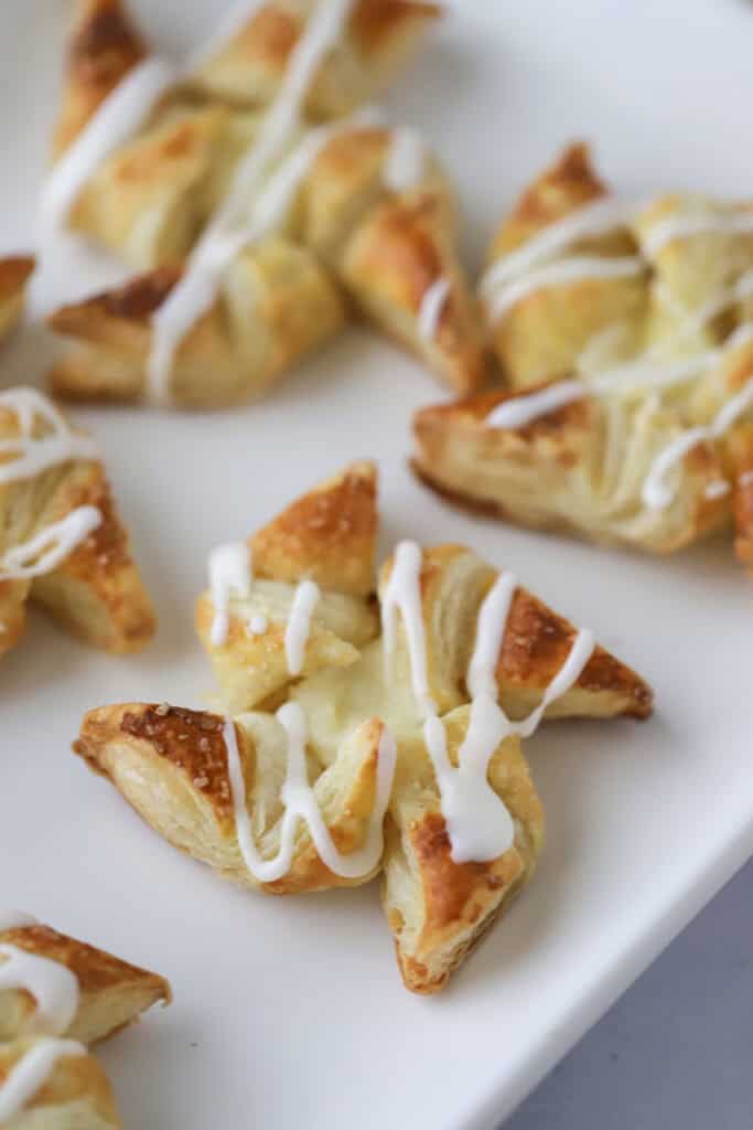 A platter with cream cheese danish made with puff pastry and drizzled with vanilla glaze.