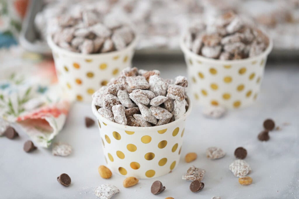 Small decorative cups filled with puppy chow that is covered in powdered sugar.