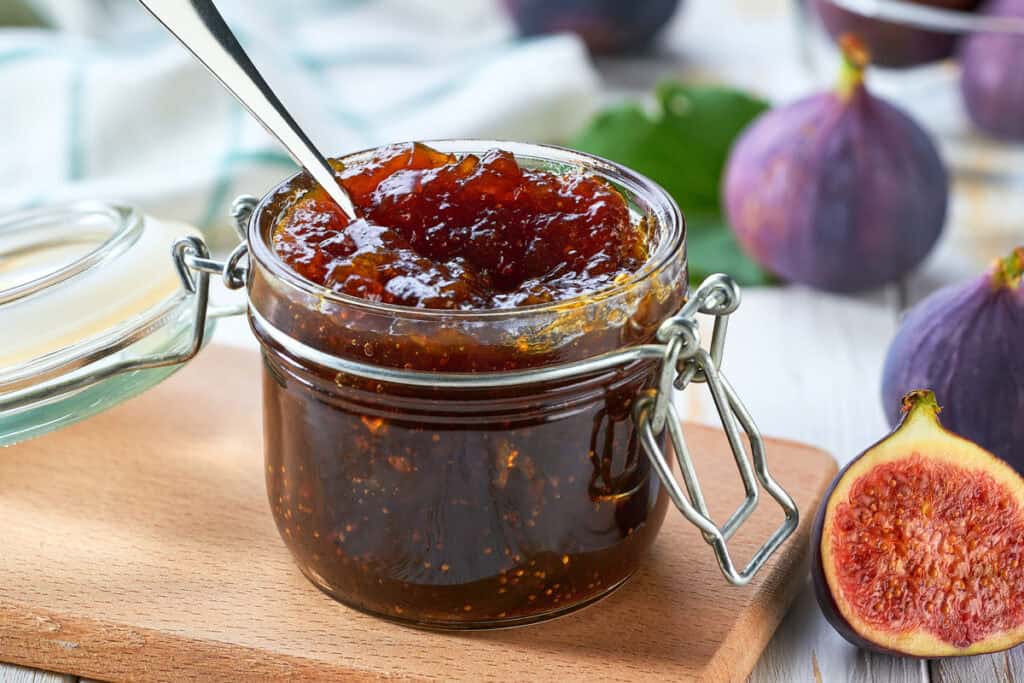 A small jar full of this fig jam recipe, sitting on a cutting board.