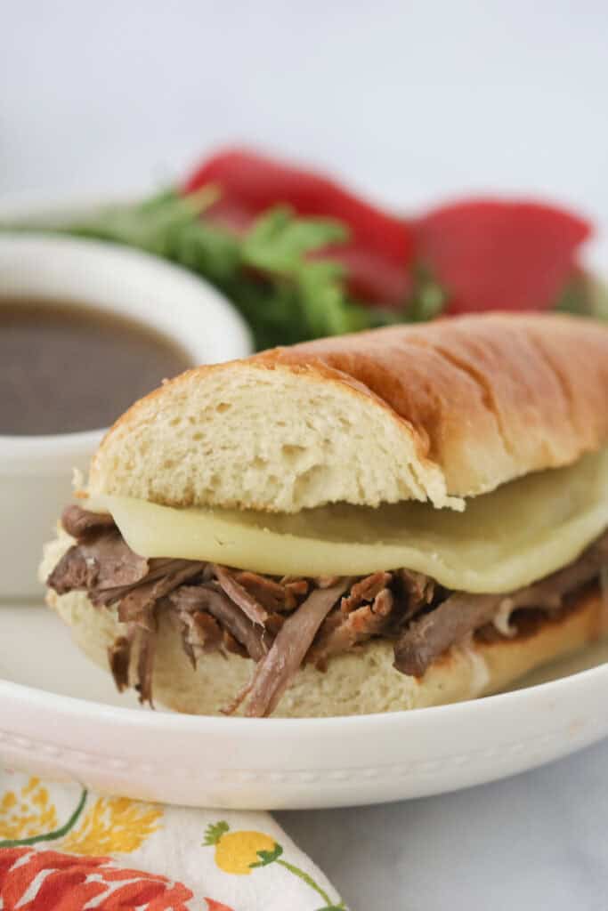 A serving plate with a French Dip Sandwich that is made with slow cooked beef and cheese.