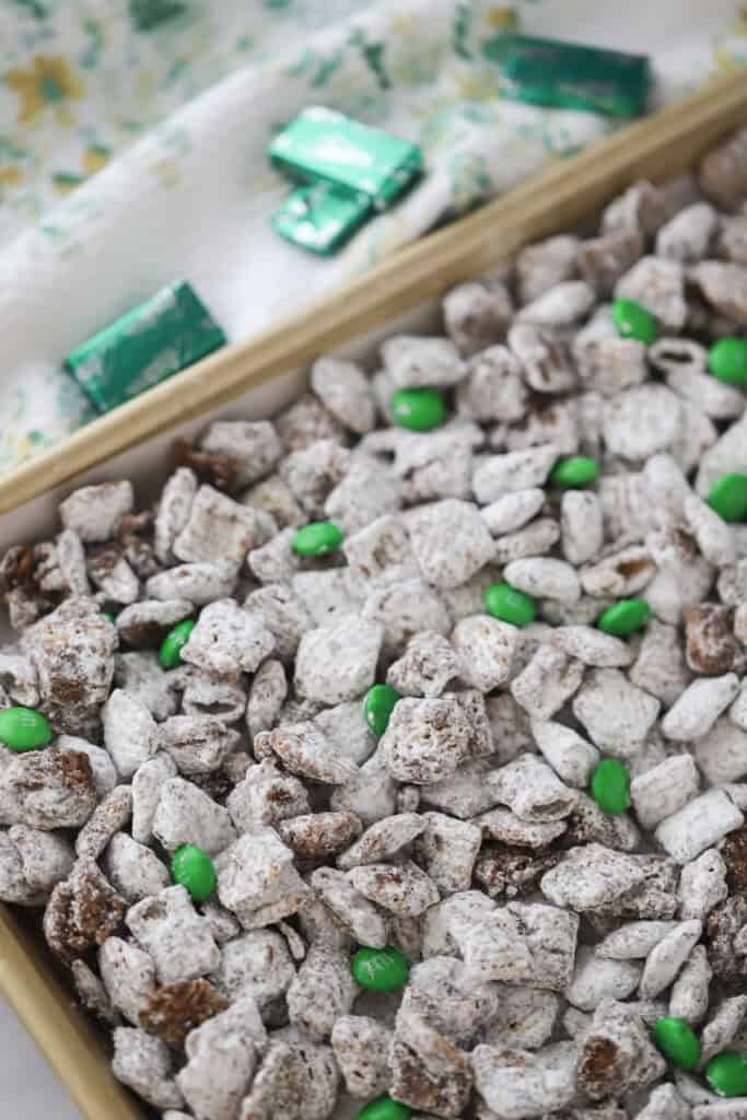 A container filled with mint puppy chow and green M&Ms.