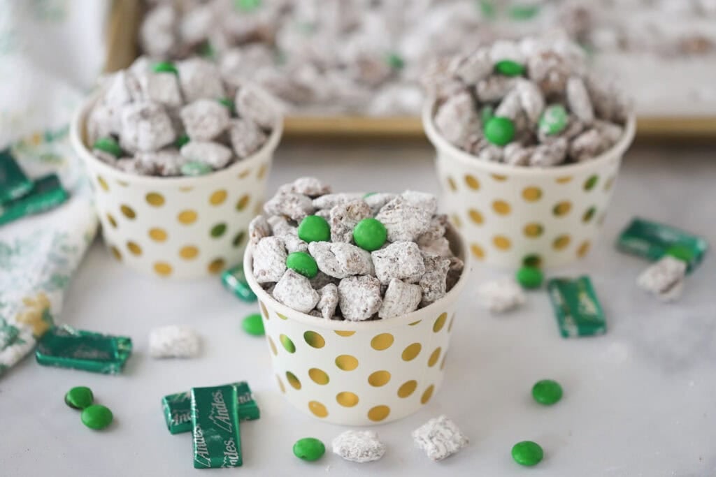 Individual cups full of mint puppy chow surrounded by Andes Chocolate Mints.