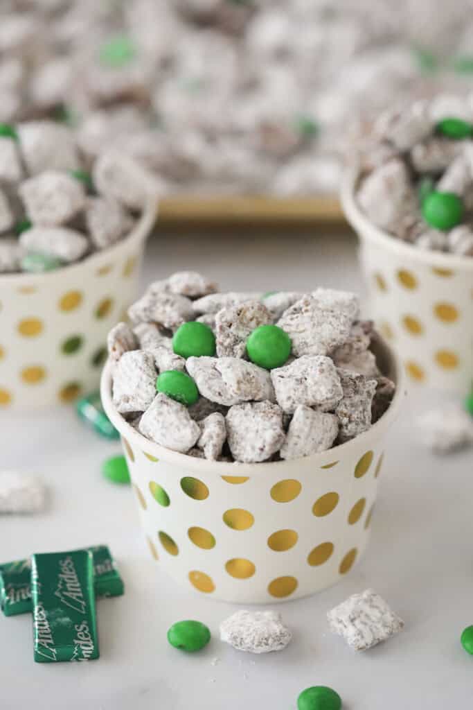 Small decorative cups full of chocolate mint muddy buddies and green M&Ms.