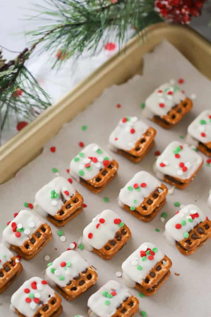 White chocolate covered Rolo pretzels on a baking sheet covered with parchment paper; topped with red and green sprinkles.