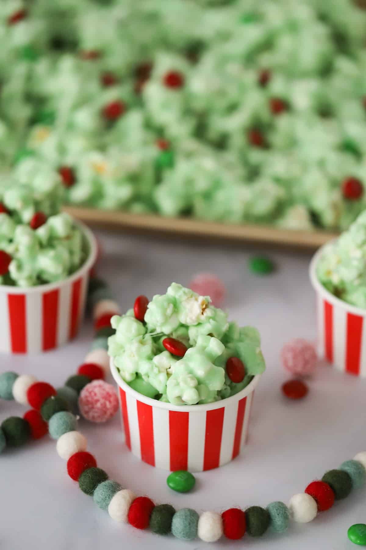 Small decorative cups full of green Grinch Popcorn that has red candy M&Ms inside, perfect for a festive holiday snack.