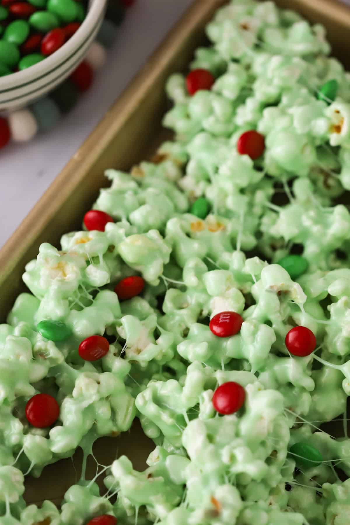 A baking sheet with a generous layer of green Grinch popcorn mixed with vibrant red M&Ms, cooling and ready to be served.