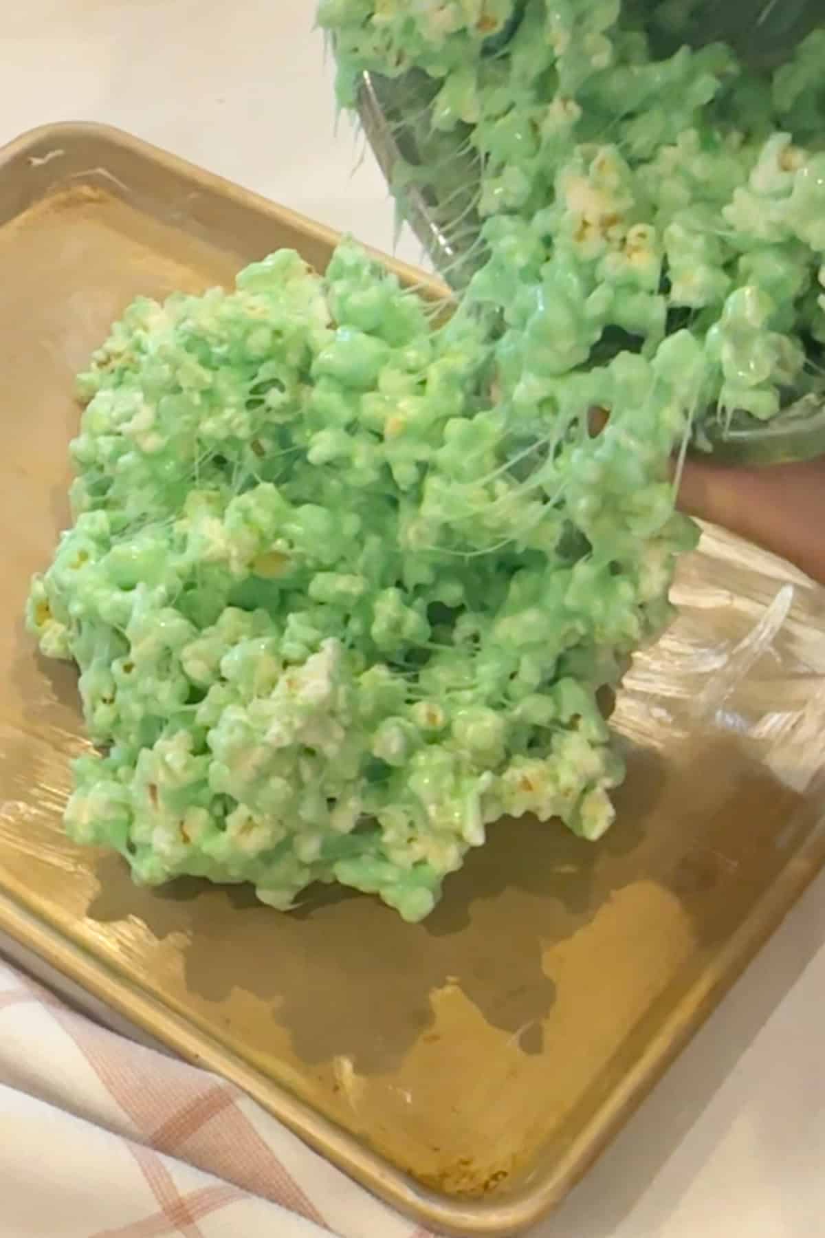 Pouring green Grinch popcorn mixture out onto a greased baking sheet to cool and set.