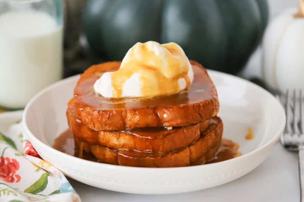 A white serving bowl full of French toast topped with whipped cream and homemade syrup.