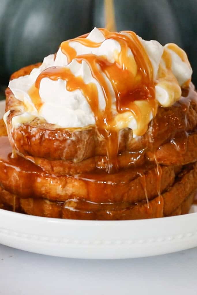 A stack of slices of pumpkin French toast topped with whipped cream and syrup.