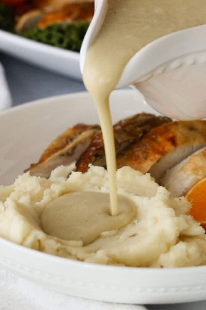 A gravy boat pouring turkey gravy over a mound of mashed potatoes on a plate.