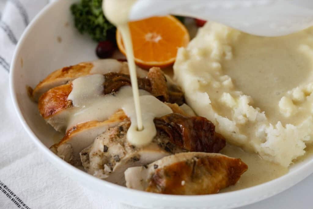 Pouring gravy over a plate of sliced turkey and mashed potatoes.