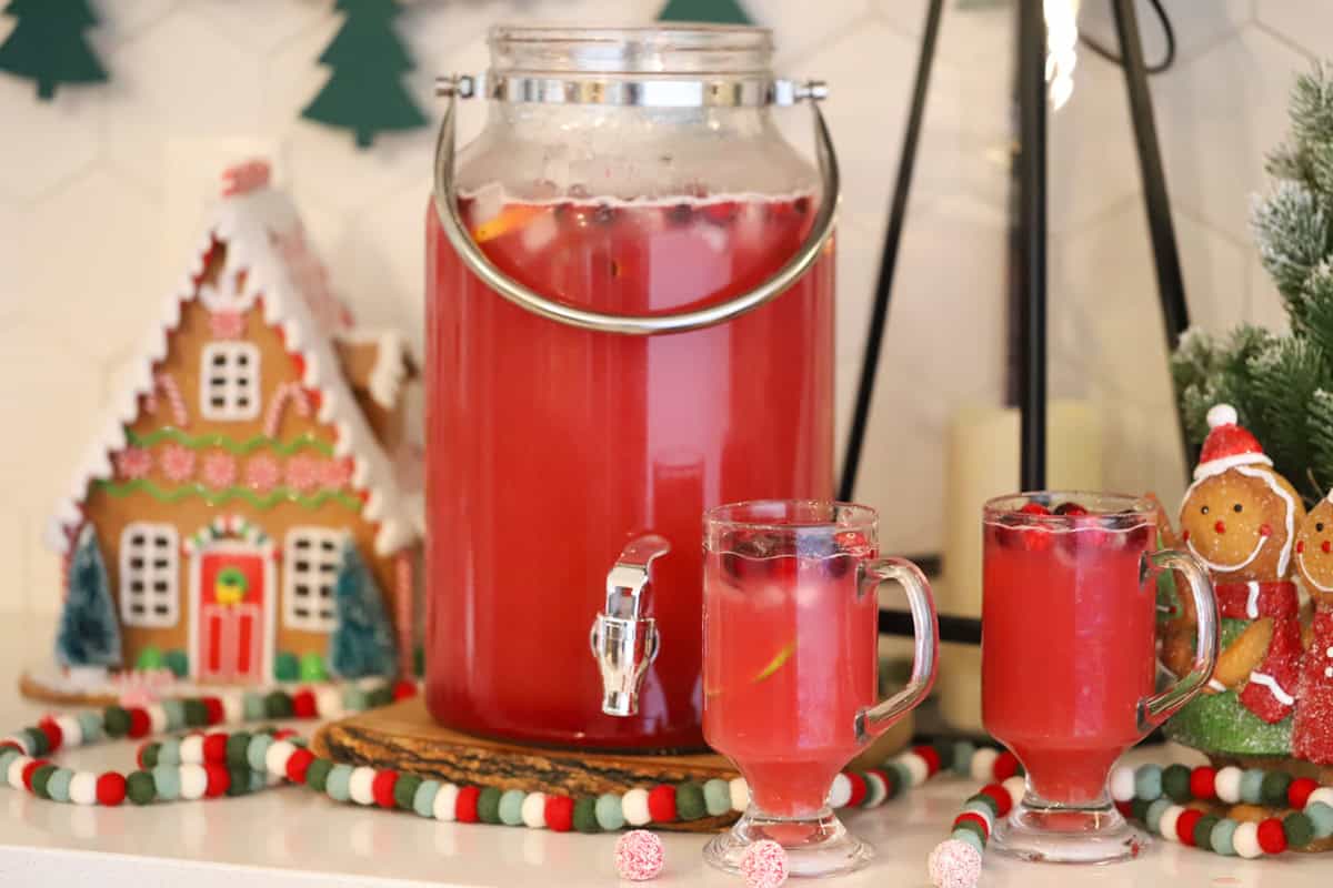 A drink dispenser full of this non alcoholic Christmas holiday punch made with cranberry and orange juices.