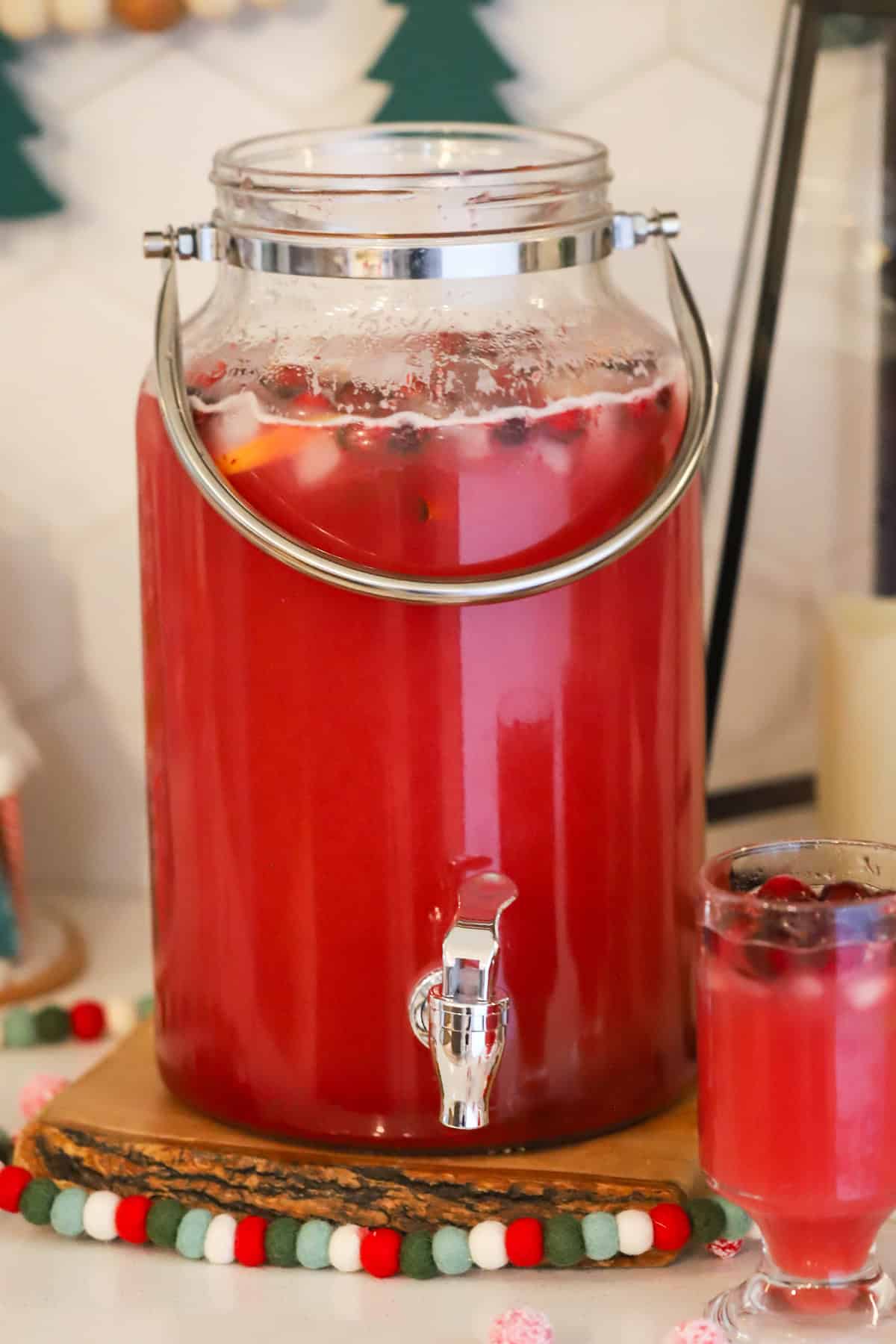 Sparkling Cranberry Orange Punch recipe inside a large drink dispenser with Christmas decorations on the table.