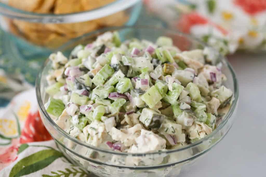 A glass serving bowl full of dick pickle chicken salad.