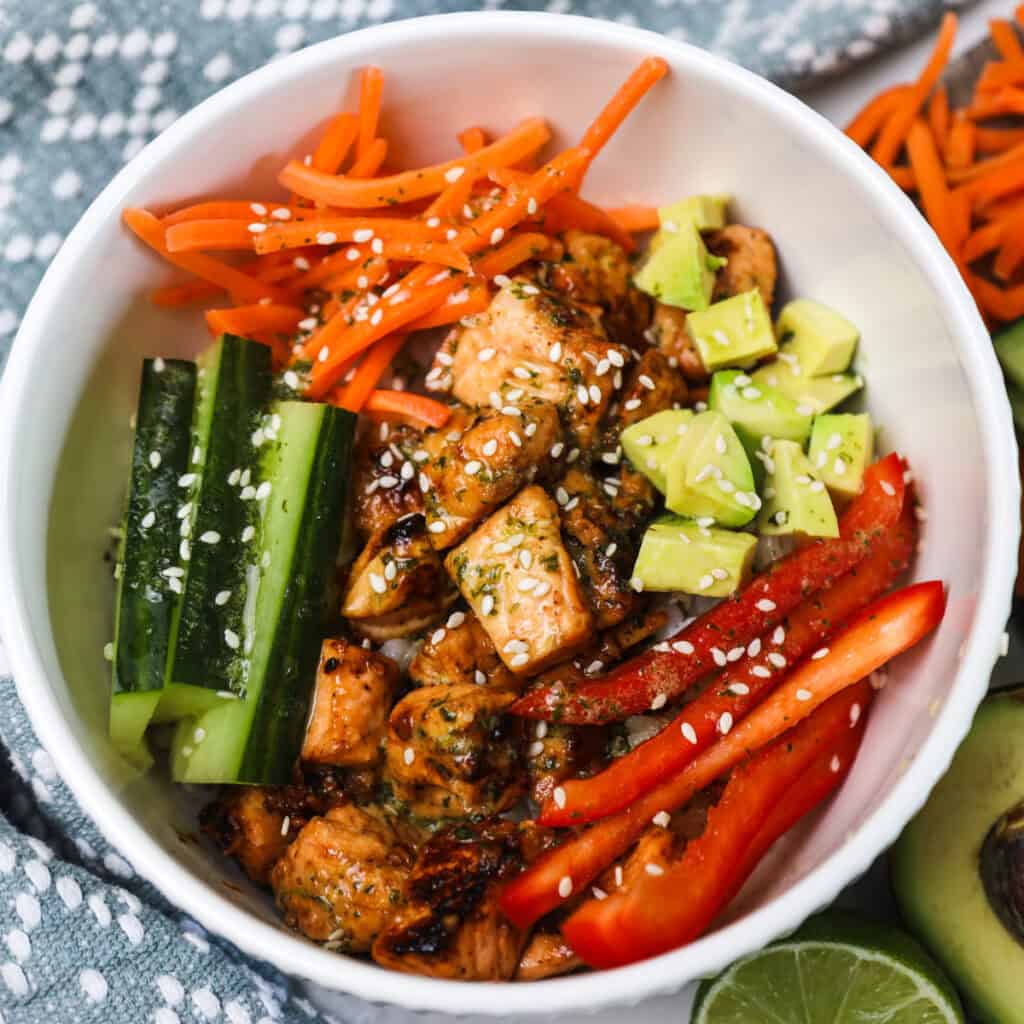 A honey glazed salmon bowl filled with honey soy glazed salmon, carrots, cucumber, avocado, peppers, and sesame seeds.