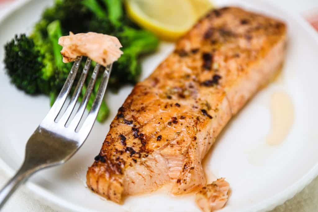 Flaky baked salmon on a white dinner plate with a side of broccoli.