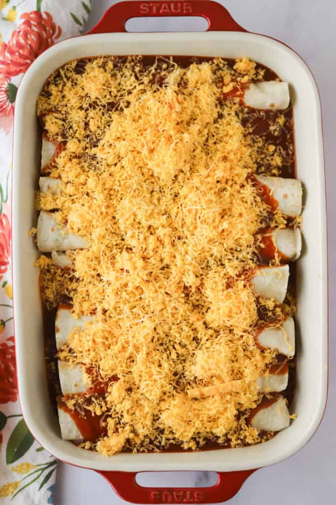 A pan of red enchiladas with shredded cheese, ready to be baked
