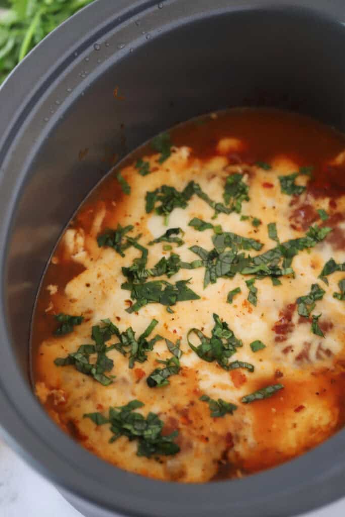 A slow cooker full of chicken Parmesan topped with melted cheese.