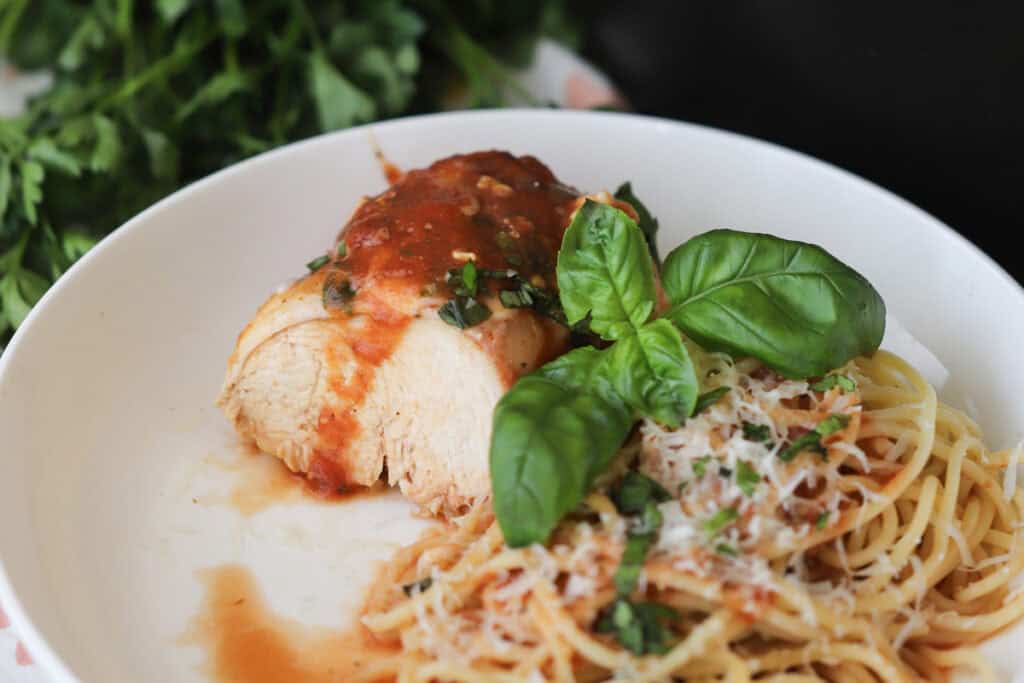 A white plate with chicken Parmesan and a side of spaghetti topped with basil.