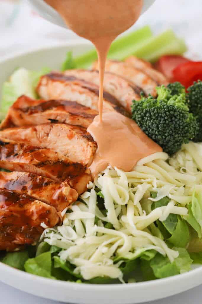Buffalo ranch dressing being poured over the top of a grilled chicken salad.