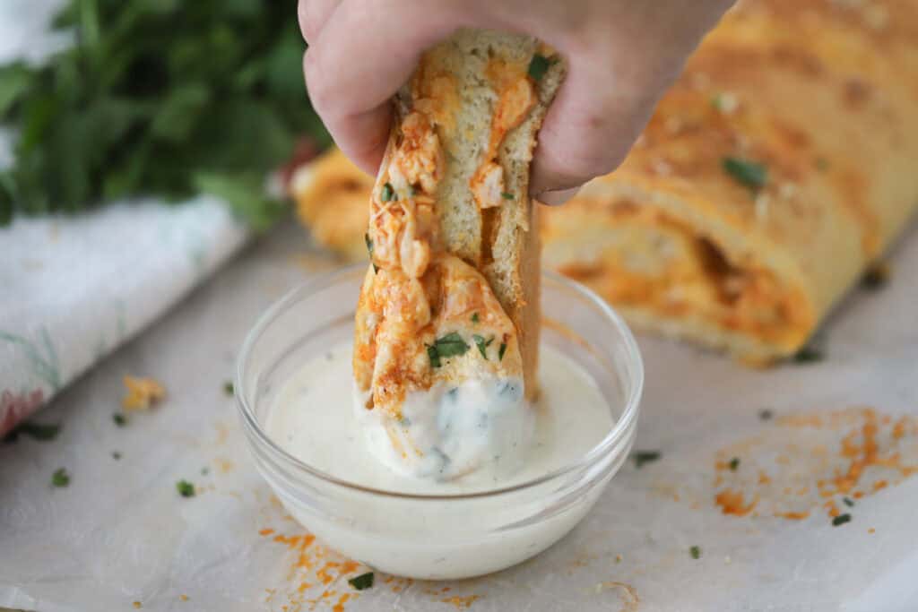 A hand dipping stromboli into ranch dressing.