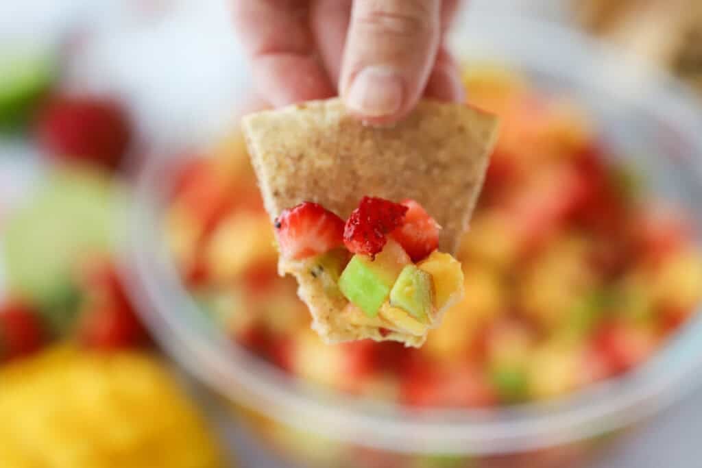 A hand holding a cinnamon chip with fruit salsa.