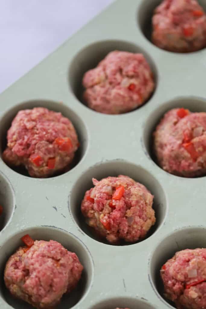 Meatloaf mixture inside a muffin pan read to bake.