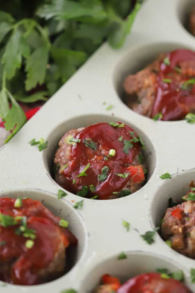 Mini meatloaves in a cupcake tin, topped with tomato sauce.