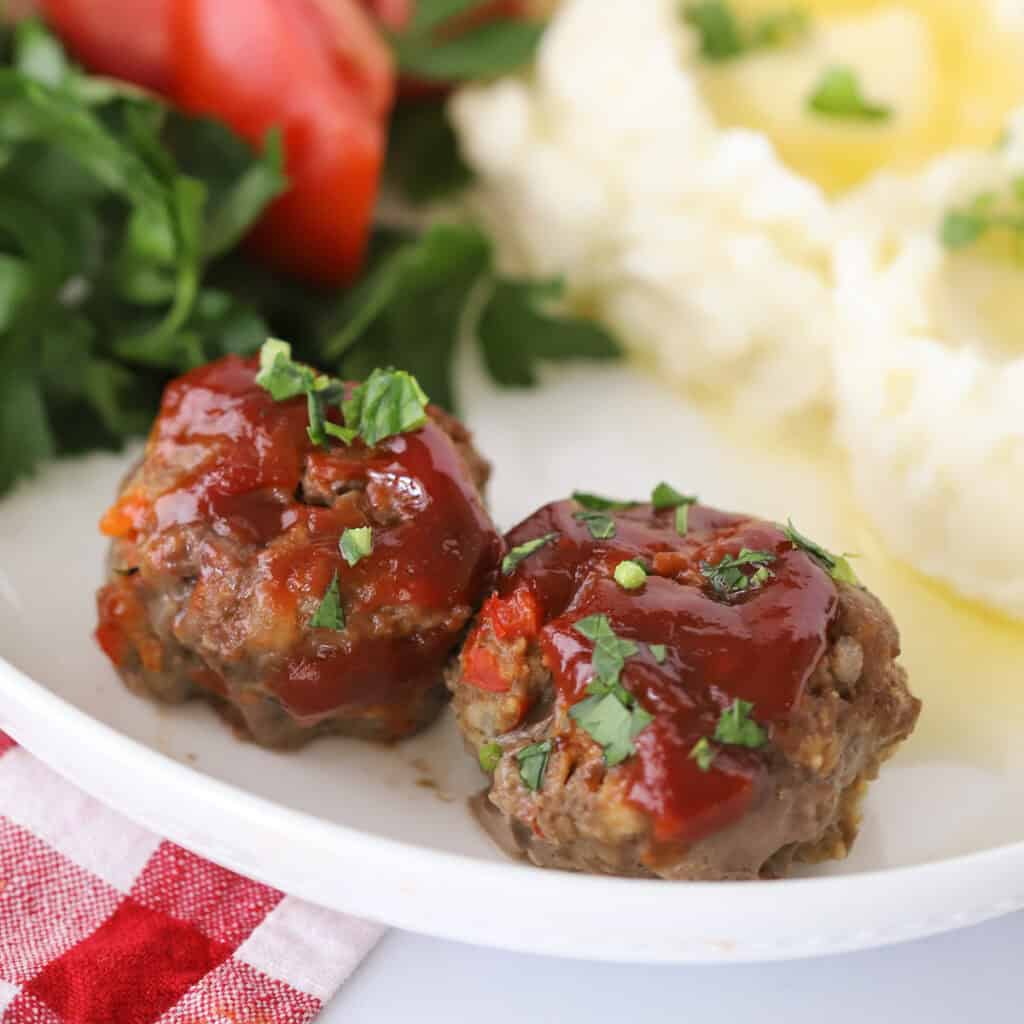 Mini meatloaf topped with tomato sauce, sitting on. a white plate.