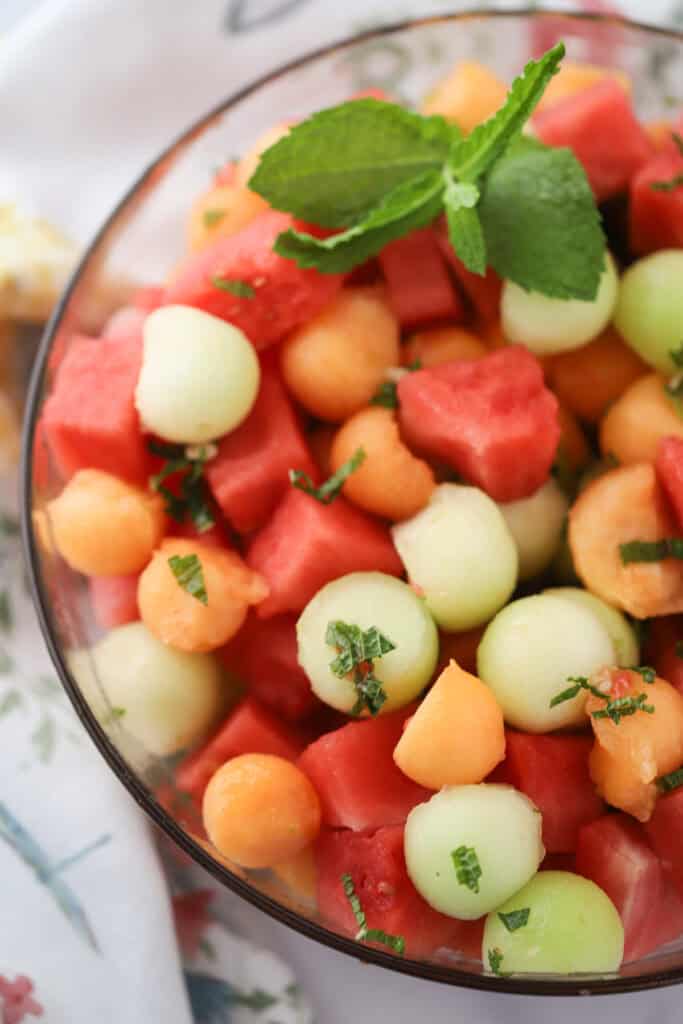 Melon salad in a glass bowl, topped with fresh mint.