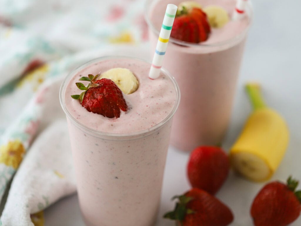 Strawberry banana smoothies with fresh strawberries and bananas in the background.