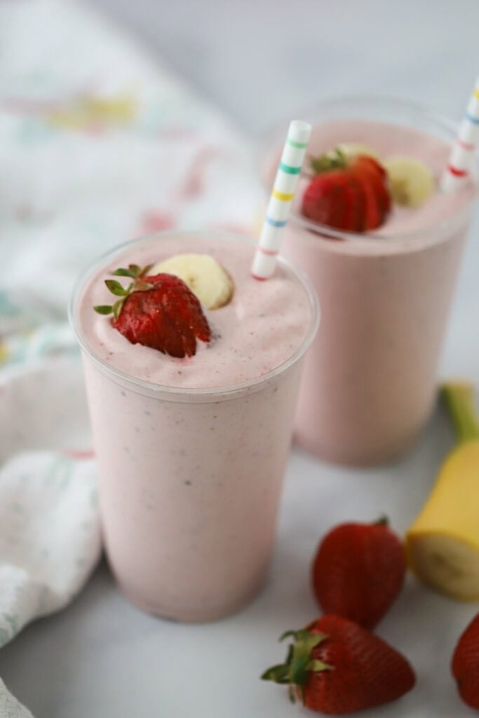 Two strawberry and banana protein smoothies with straws.