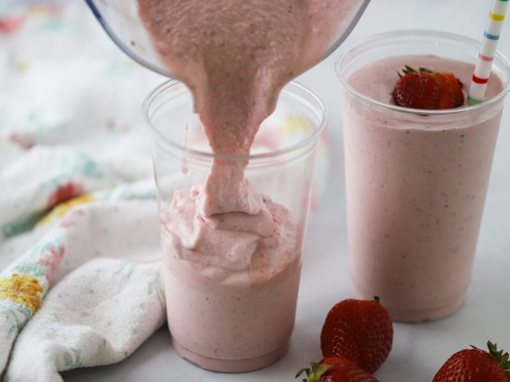 Pouring this strawberry protein shake into plastic cups.