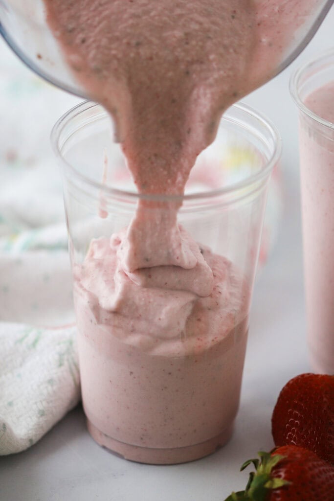 Pouring a strawberry and banana smoothie into a plastic cup.