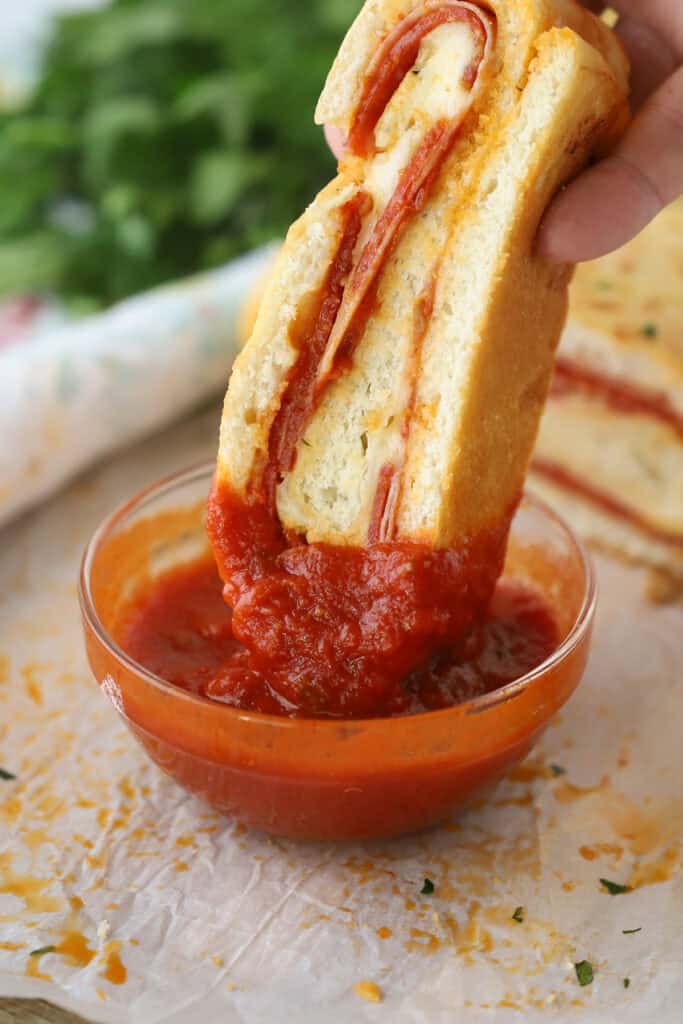 A hand dipping a slice of stromboli into marinara sauce.