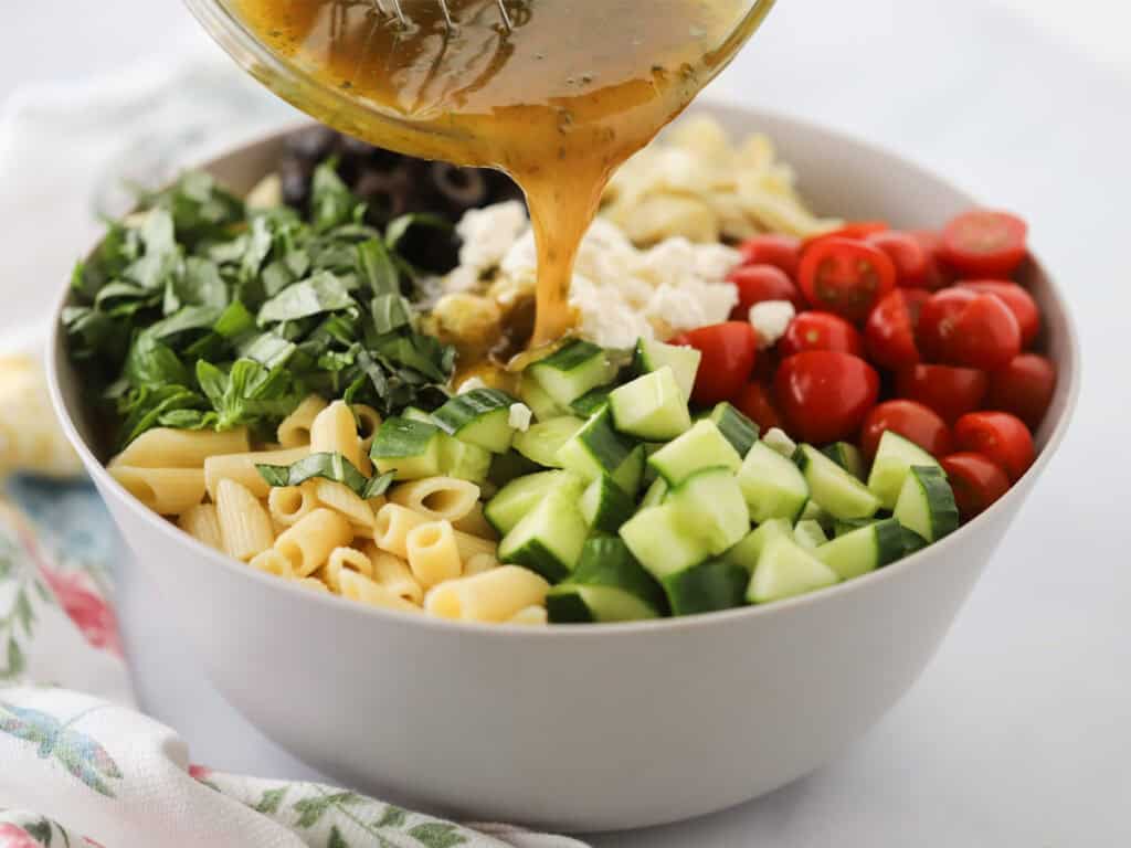 Pouring dressing over Greek pasta salad ingredients.