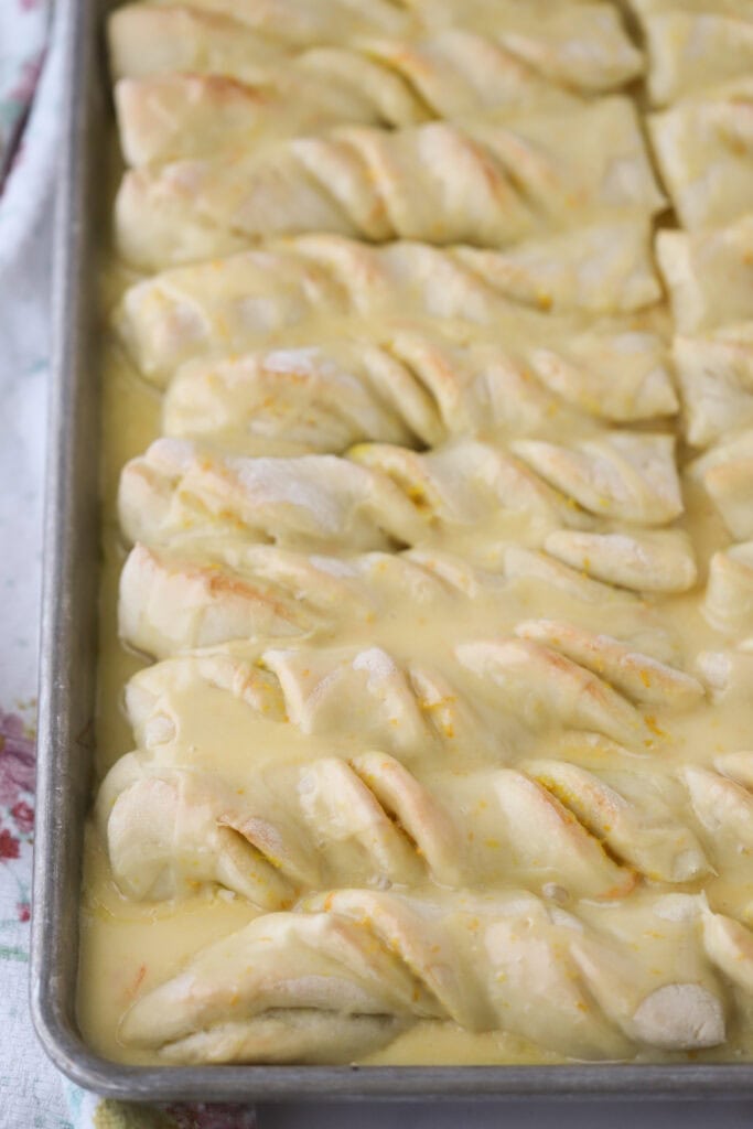 A baking sheet full of orange twist breadsticks covered in orange glaze.