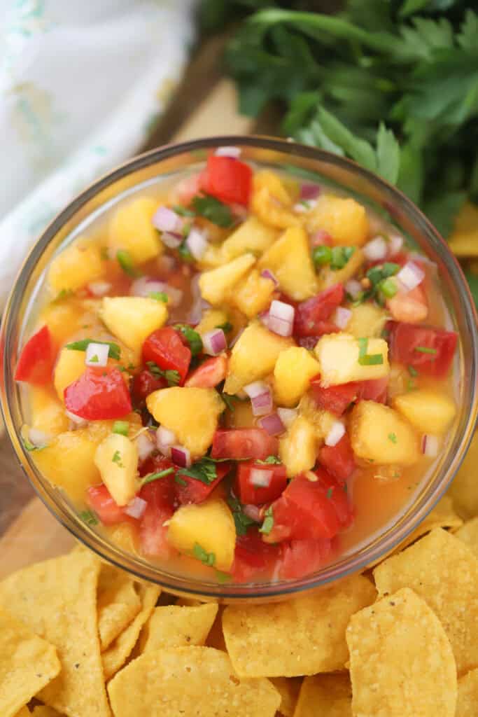 A small glass bowl full of peach salsa made with red onions, tomatoes, and cilantro.