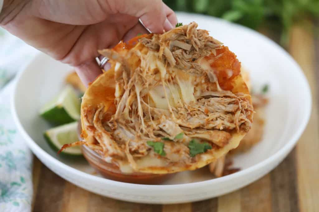 A hand opening up a cooked pork birria taco filled with gooey cheese.