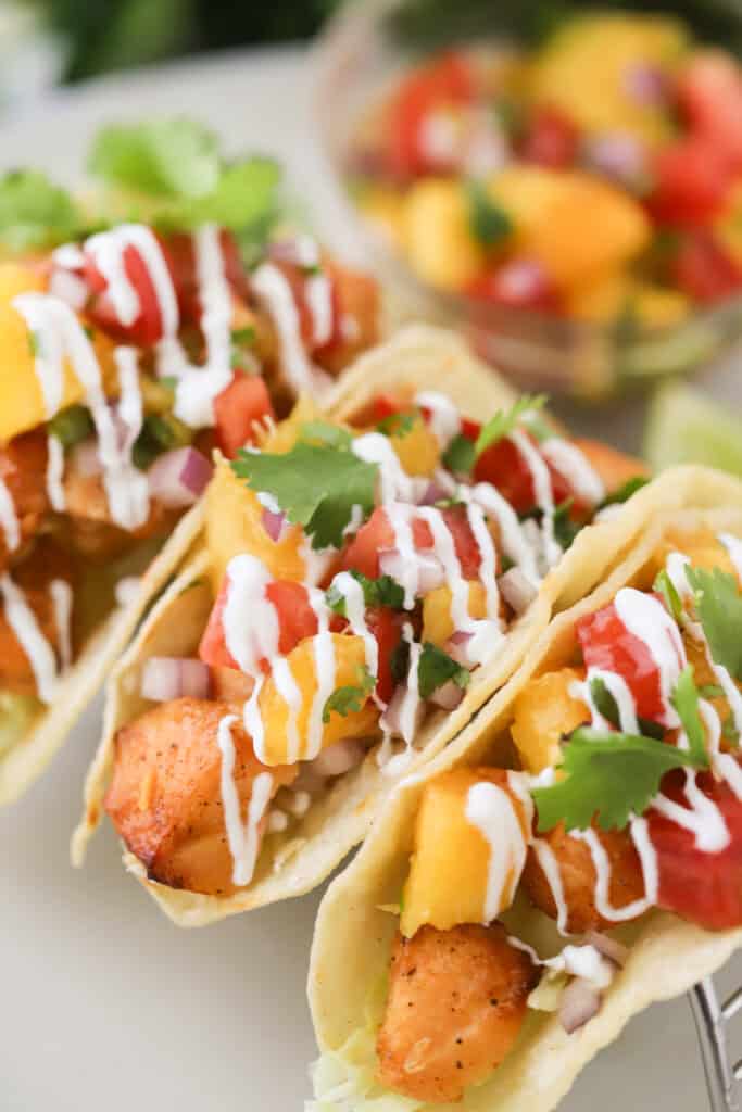A counter with salmon fish tacos topped with lime crema and peach salsa.