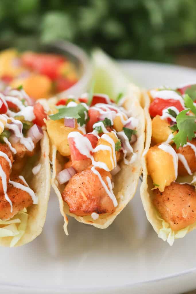 Fish tacos filled with air fried salmon bites, peach salsa, and lime crema.