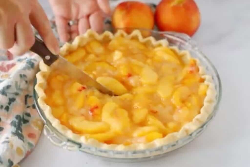 cutting a fresh peach pie with a knife, chilled and ready to serve with whipped cream or ice cream. 