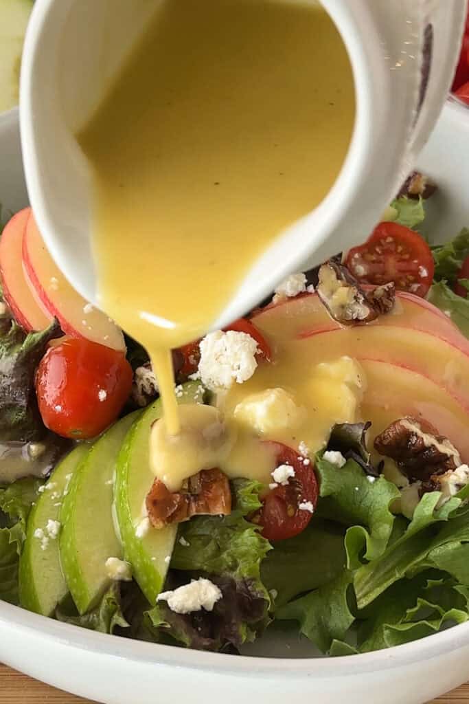 A small ramekin pouring honey mustard dressing over the top of a fall chicken salad.