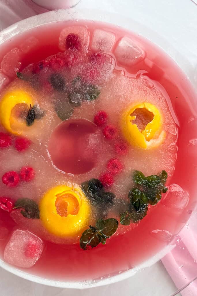 A large punch bowl with an ice ring in the center frozen with lemon rosettes, raspberries, and mint leaves.