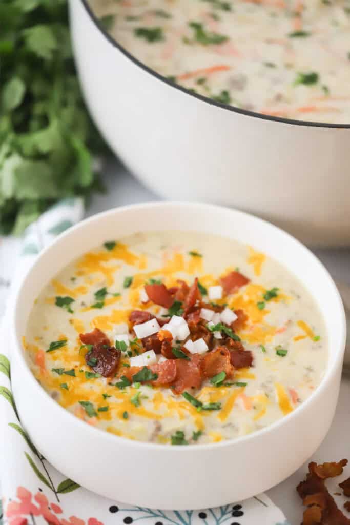 A white bowl full of this easy cheeseburger soup, topped with bacon bits, cheese, and diced onions.