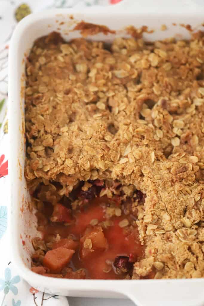 A baking dish with cranberry crisp that has a portion removed.