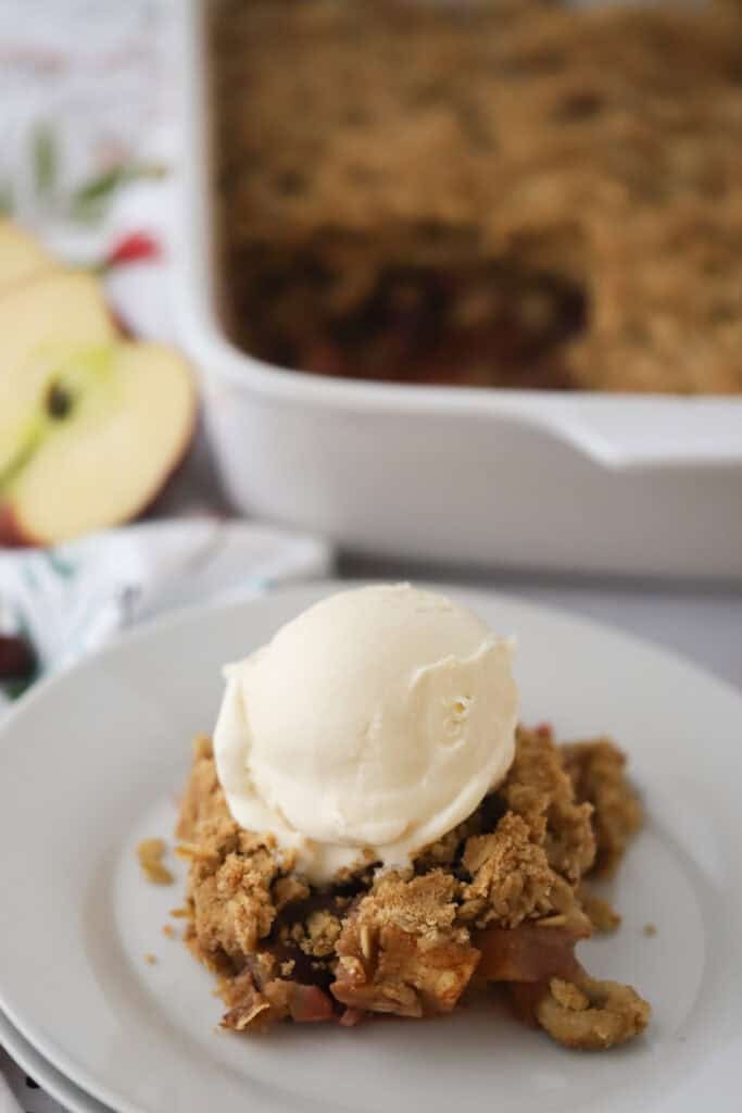 A white dessert plate with cranberry apple crisp topped with vanilla ice cream.