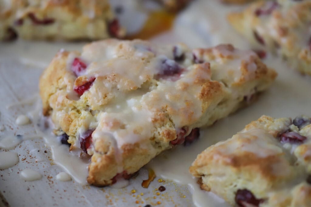 Freshly baked cranberry scones on a baking sheet, topped with orange glaze.